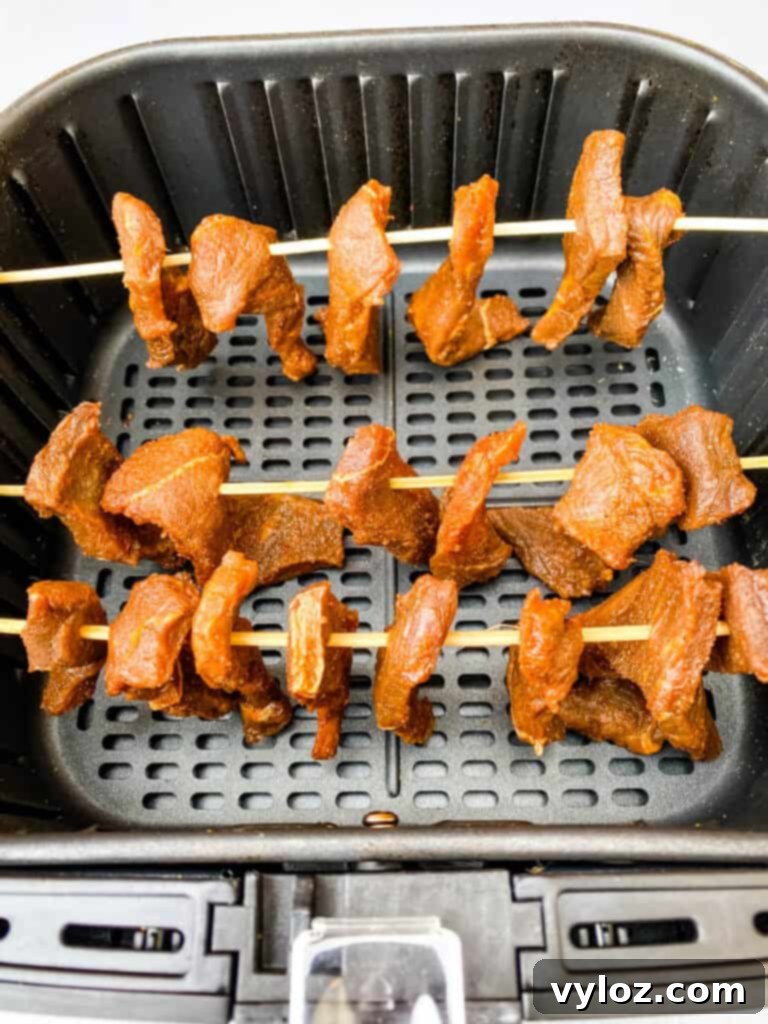 Beef jerky strips neatly hung on bamboo skewers inside an air fryer, cooking to perfection