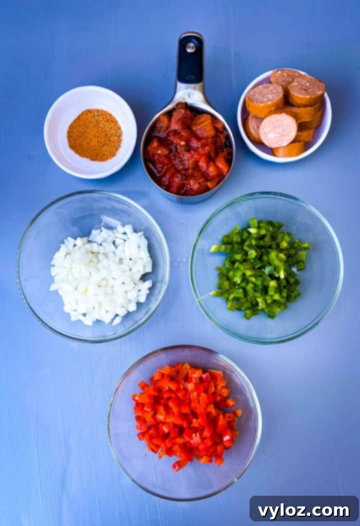 Individual bowls of Cajun seasoning, chopped onions, chopped red and green peppers, sliced andouille sausage, and fire roasted tomatoes, prepped for the pasta dish