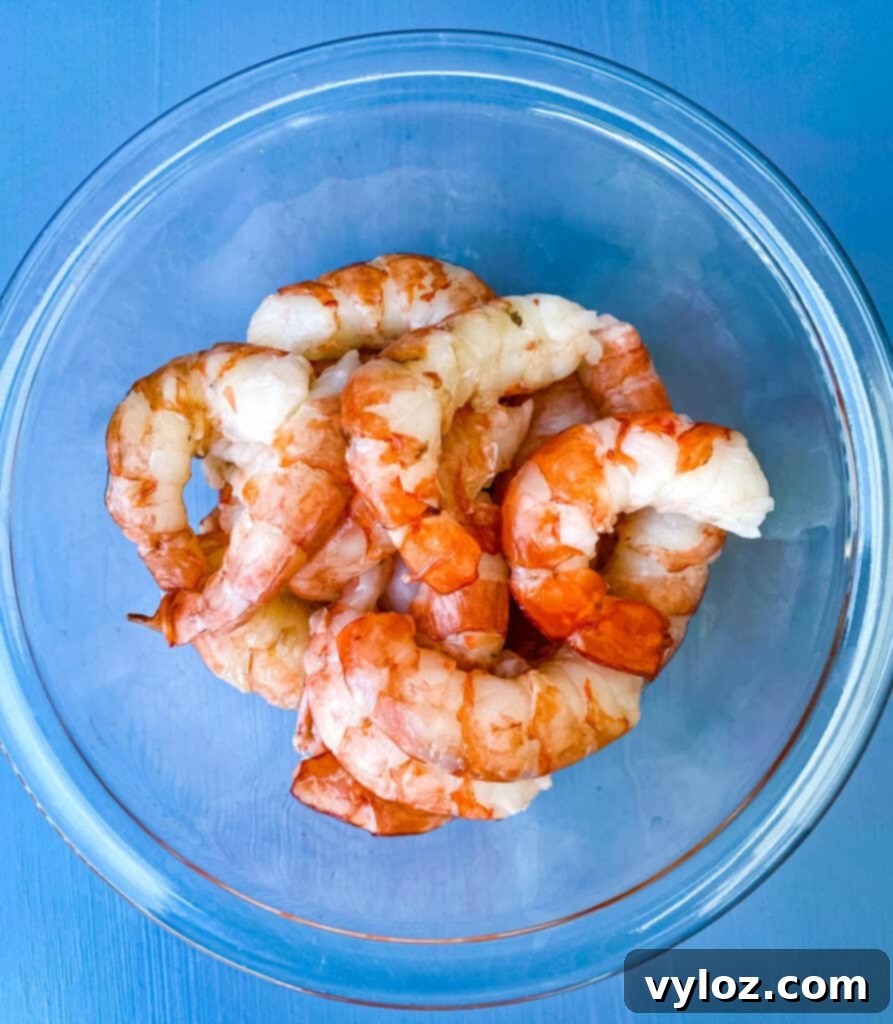 Fresh, raw wild-caught shrimp in a clear glass bowl, seasoned and ready for cooking