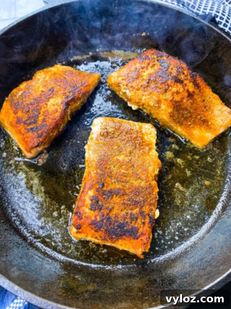 blackened salmon cooking in a cast iron skillet