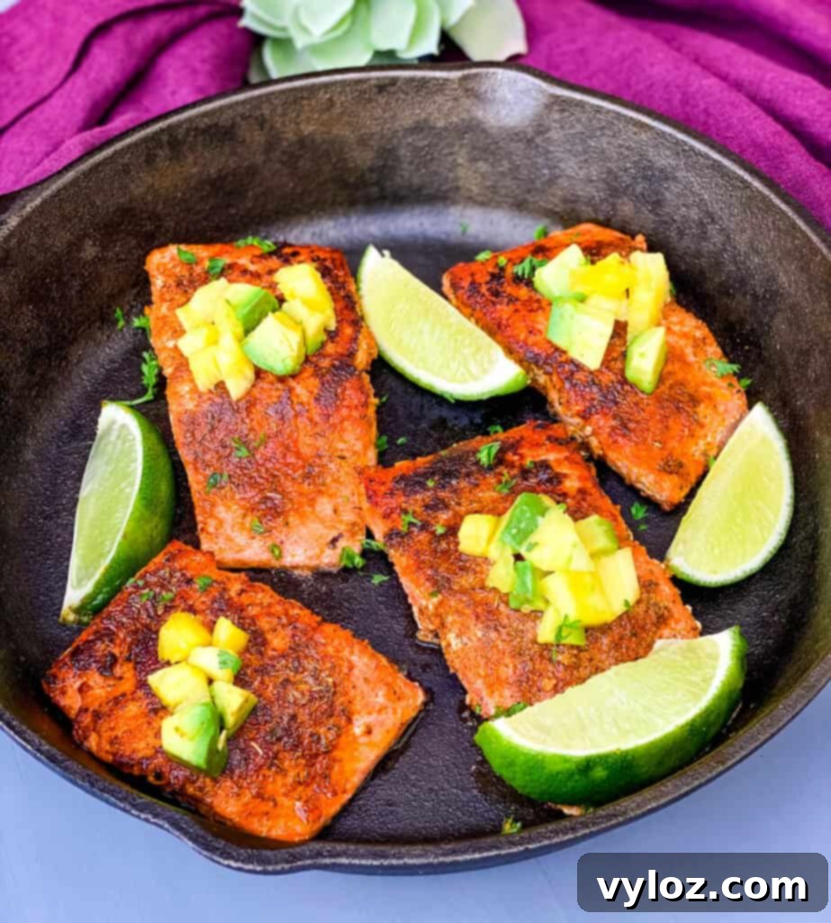 blackened salmon in a cast iron skillet topped with pineapple and avocado