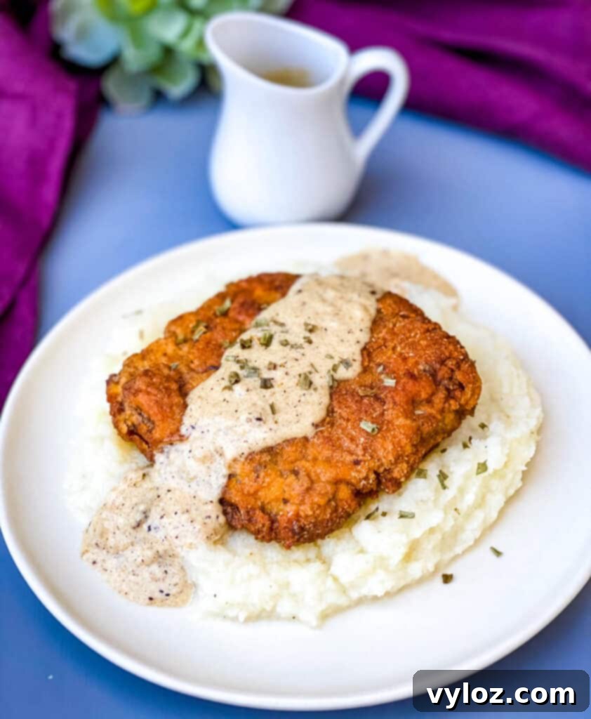 Southern Keto Chicken Fried Steak and Gravy 2 keto low carb chicken fried steak with country gravy on a bed of cauliflower mash on a white plate