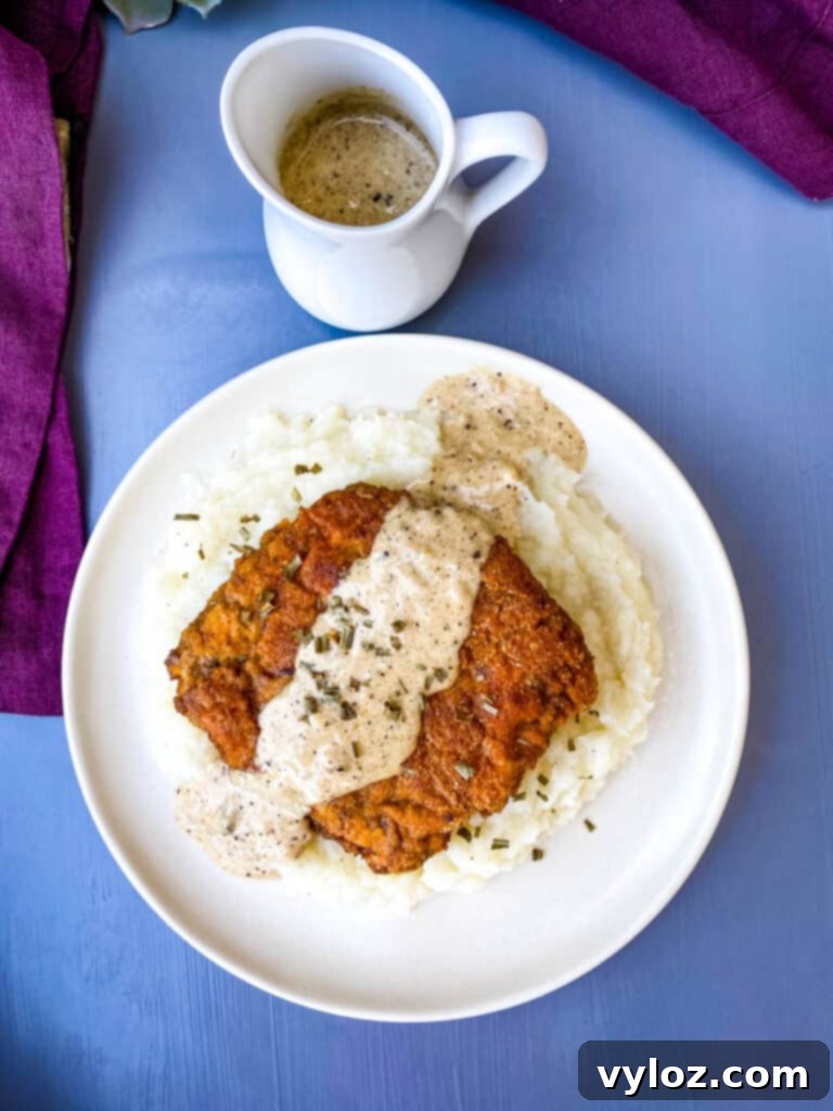 Southern Keto Chicken Fried Steak and Gravy 11 keto low carb chicken fried steak with country gravy on a bed of cauliflower mash on a white plate