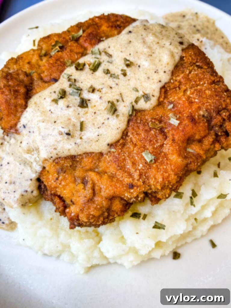 Southern Keto Chicken Fried Steak and Gravy 12 keto low carb chicken fried steak with country gravy on a bed of cauliflower mash on a white plate