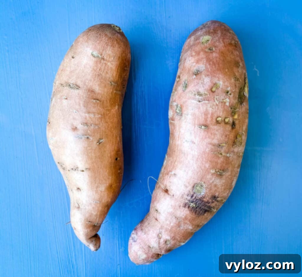 Crispy Air Fryer Sweet Potato Chips 3 Two whole raw sweet potatoes resting on a rustic wooden surface, highlighting their natural form