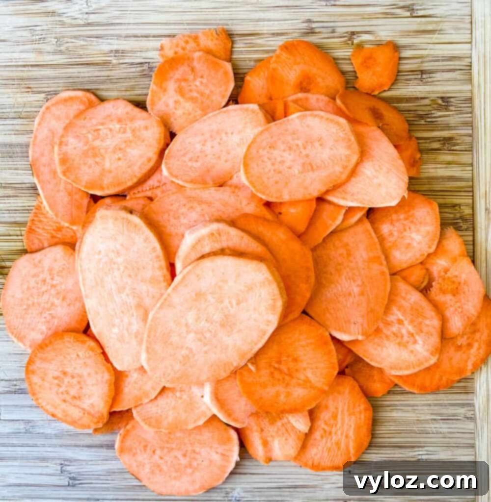 Crispy Air Fryer Sweet Potato Chips 5 Raw, thinly sliced sweet potato chips meticulously arranged on a rustic wooden cutting board