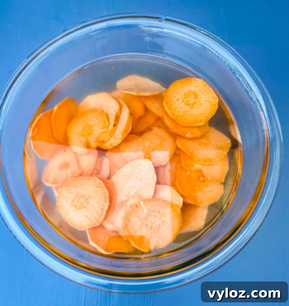Crispy Air Fryer Sweet Potato Chips 6 Thinly sliced sweet potato chips immersing in a glass bowl filled with cold water