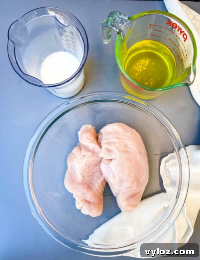 raw chicken breasts in a glass bowl, buttermilk in cup, and pickle juice in a cup