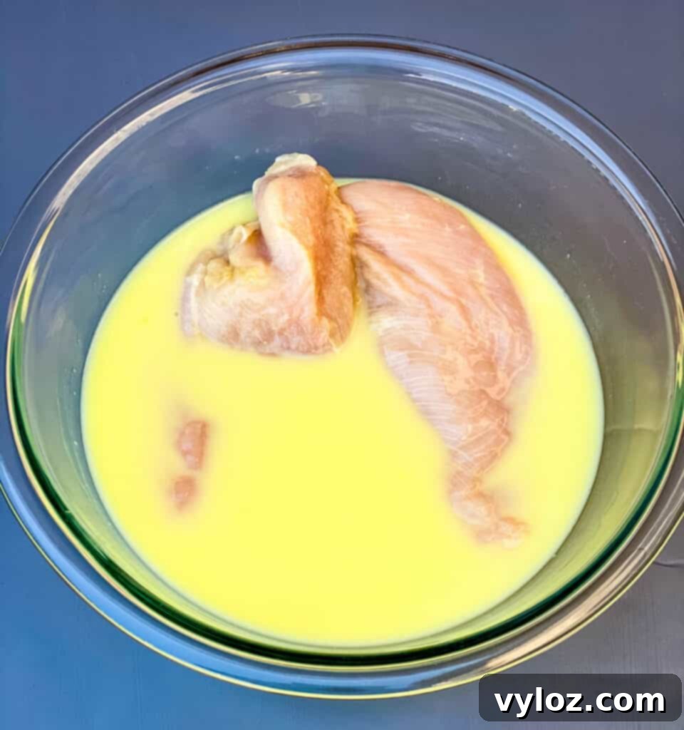 raw chicken breasts in a glass bowl with pickle juice and buttermilk