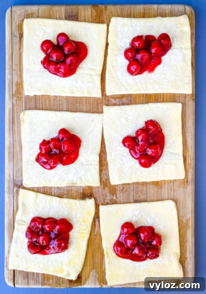 puff pastry filled with cherry pie filling on a bamboo cutting board