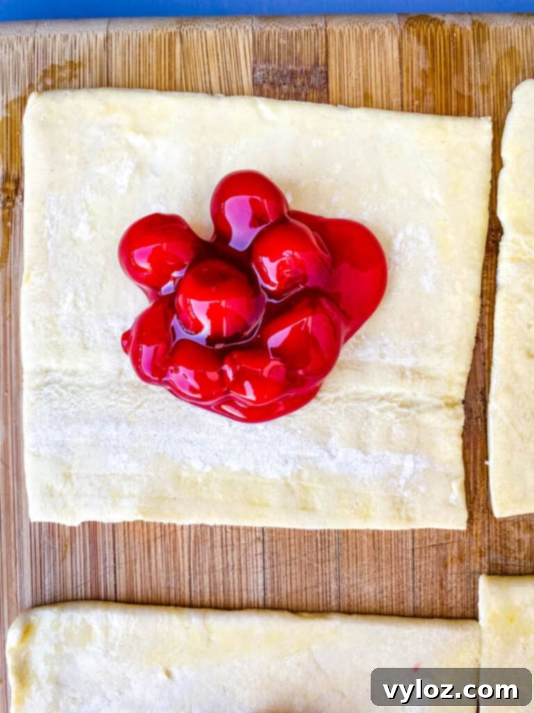 puff pastry filled with cherry pie filling on a bamboo cutting board