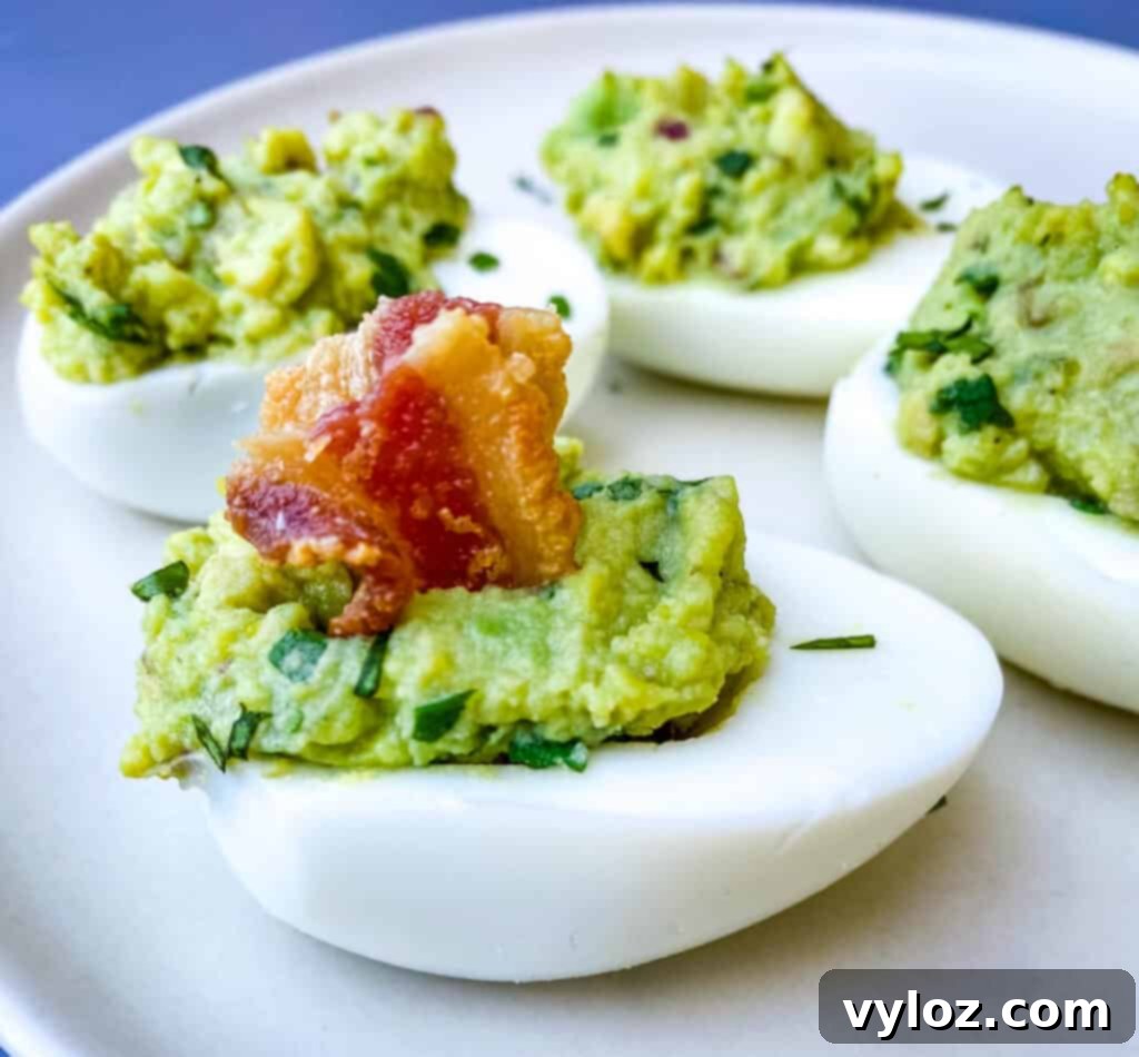 Avocado deviled eggs generously topped with crispy bacon crumbles, artfully arranged on a serving platter.
