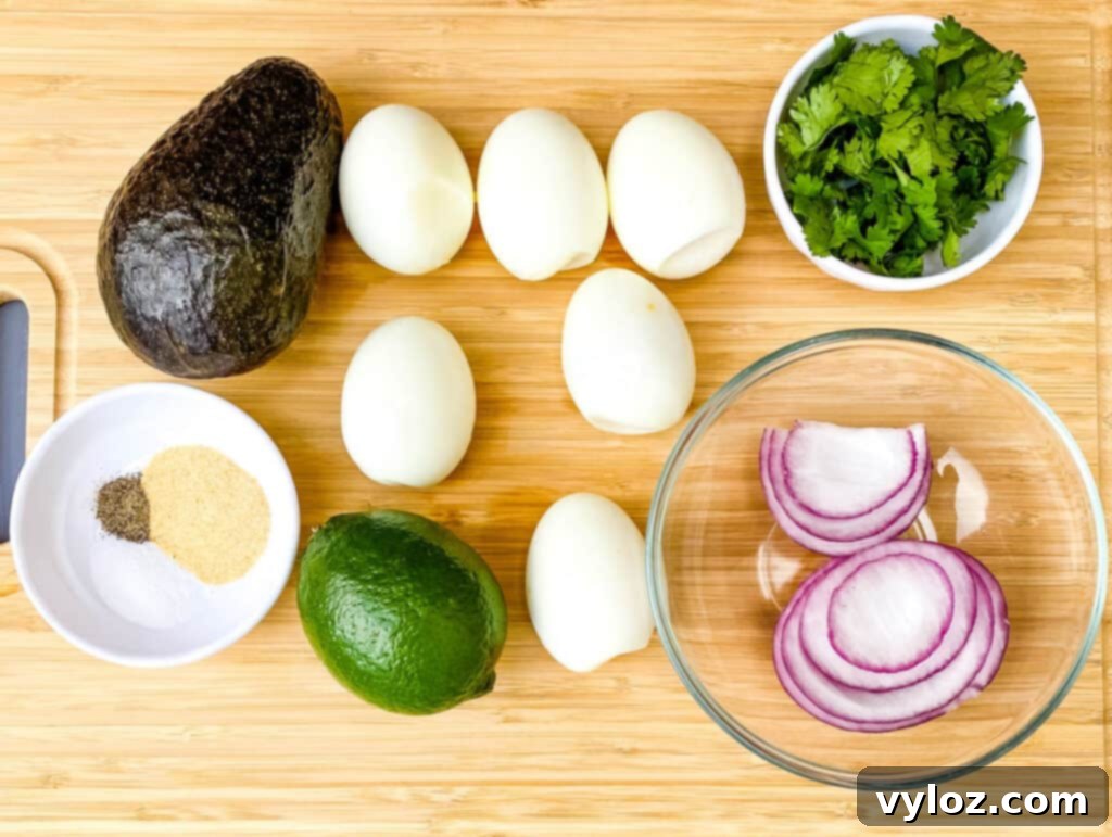 Fresh ingredients laid out for avocado deviled eggs: hard-boiled eggs, ripe avocado, vibrant red onions, and fresh cilantro leaves on a flat surface.