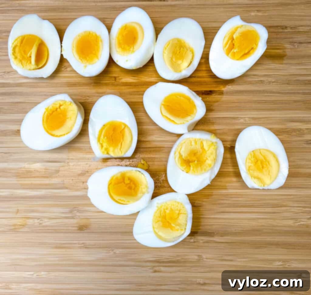 Hard-boiled eggs sliced in half, showcasing perfectly cooked yolks, arranged on a bamboo cutting board.