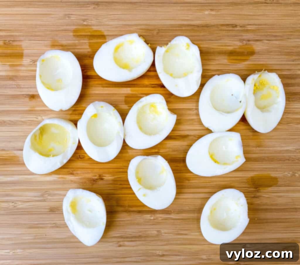 Hard-boiled eggs cut in half with the golden yolks carefully removed, ready for the deviled egg filling, on a bamboo cutting board.