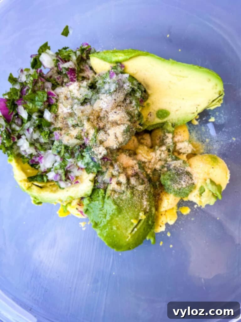 A glass bowl filled with mashed avocado, finely chopped red onions, and fresh cilantro, ready to be mixed with egg yolks.