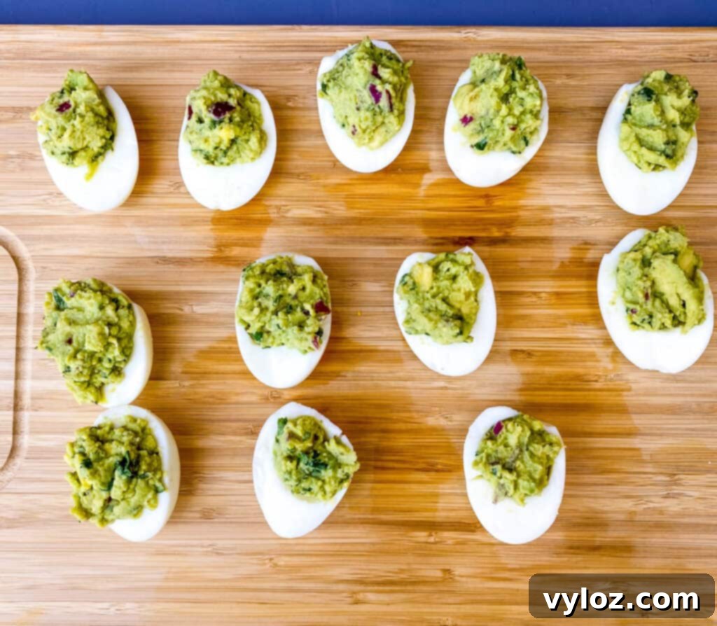 A tray of beautifully presented avocado deviled eggs, garnished with fresh herbs and a sprinkle of paprika, on a bamboo cutting board.