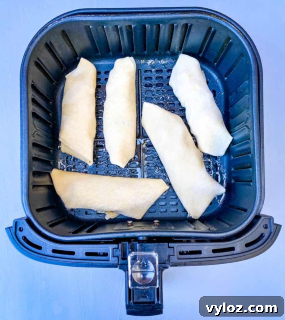 Golden brown shrimp egg rolls cooking in an air fryer basket, showcasing a healthier way to achieve crispiness.