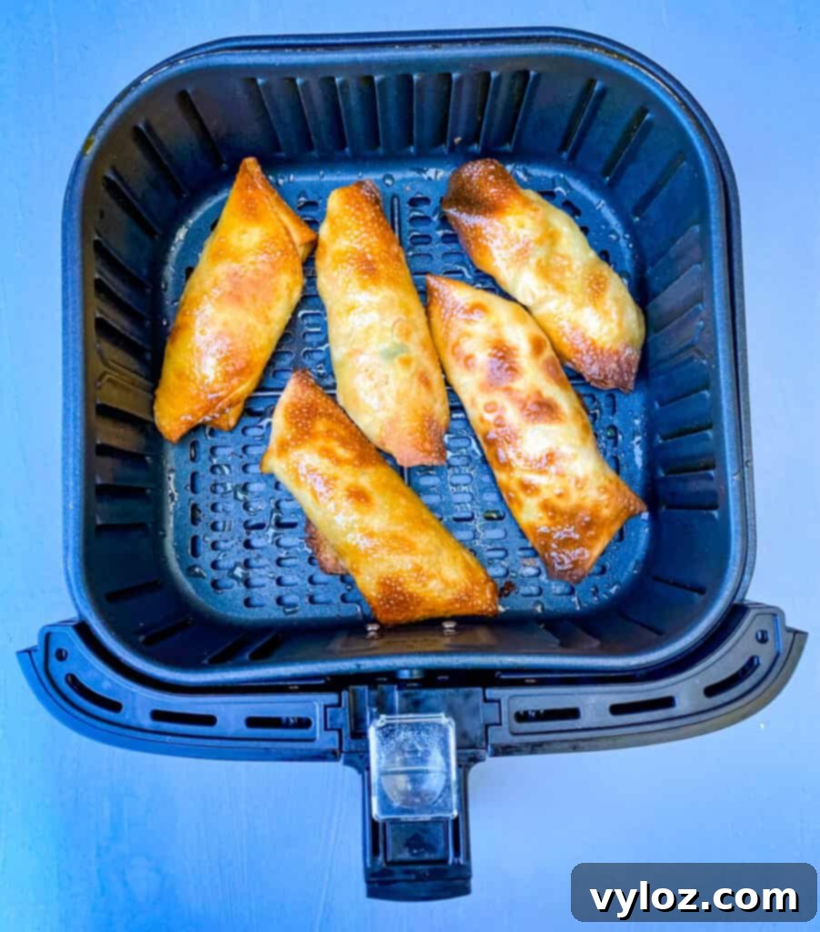 A close-up view of shrimp egg rolls cooking to a perfect golden crisp in an air fryer.