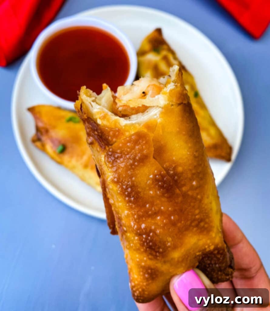 A person holding a freshly made shrimp egg roll with a delicious bite taken out, showcasing the crispy wrapper and savory filling.