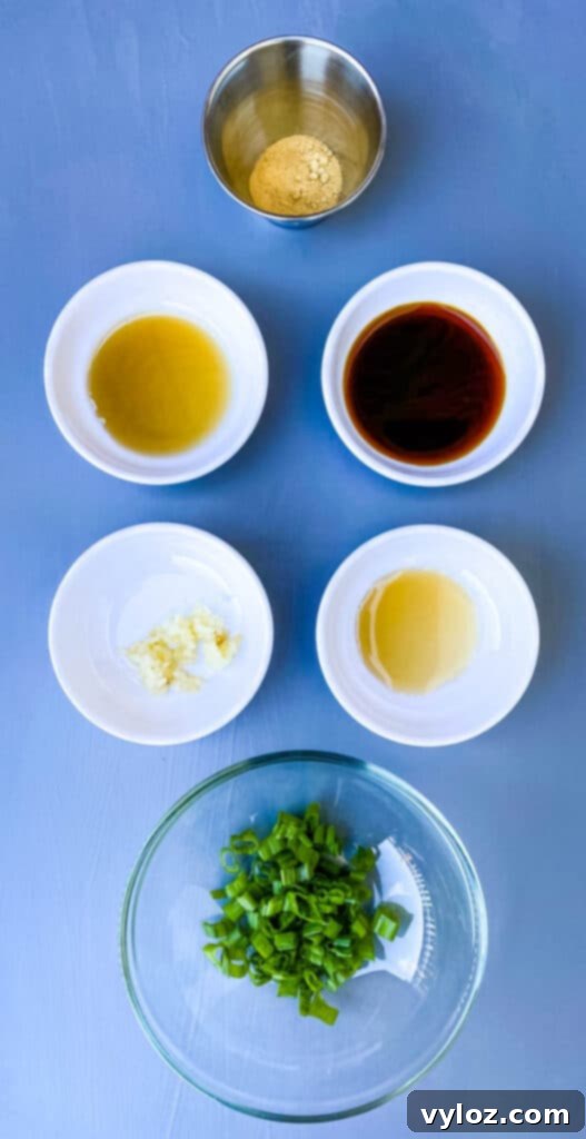 A vibrant selection of shrimp egg roll ingredients: sesame oil, savory fish sauce, minced garlic, freshly chopped green onions, dark soy sauce, and aromatic ground ginger, artfully arranged in separate small bowls.