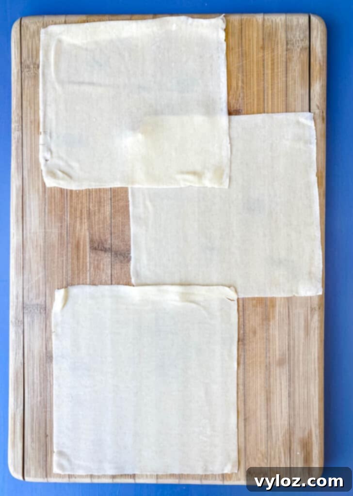 A stack of golden-yellow egg roll wrappers neatly fanned out on a wooden cutting board, ready for filling.