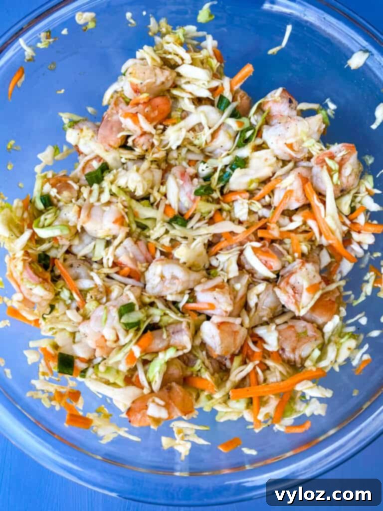A bowl filled with freshly prepared shrimp egg roll filling, featuring chopped shrimp, coleslaw mix, and vibrant seasonings, ready for wrapping.