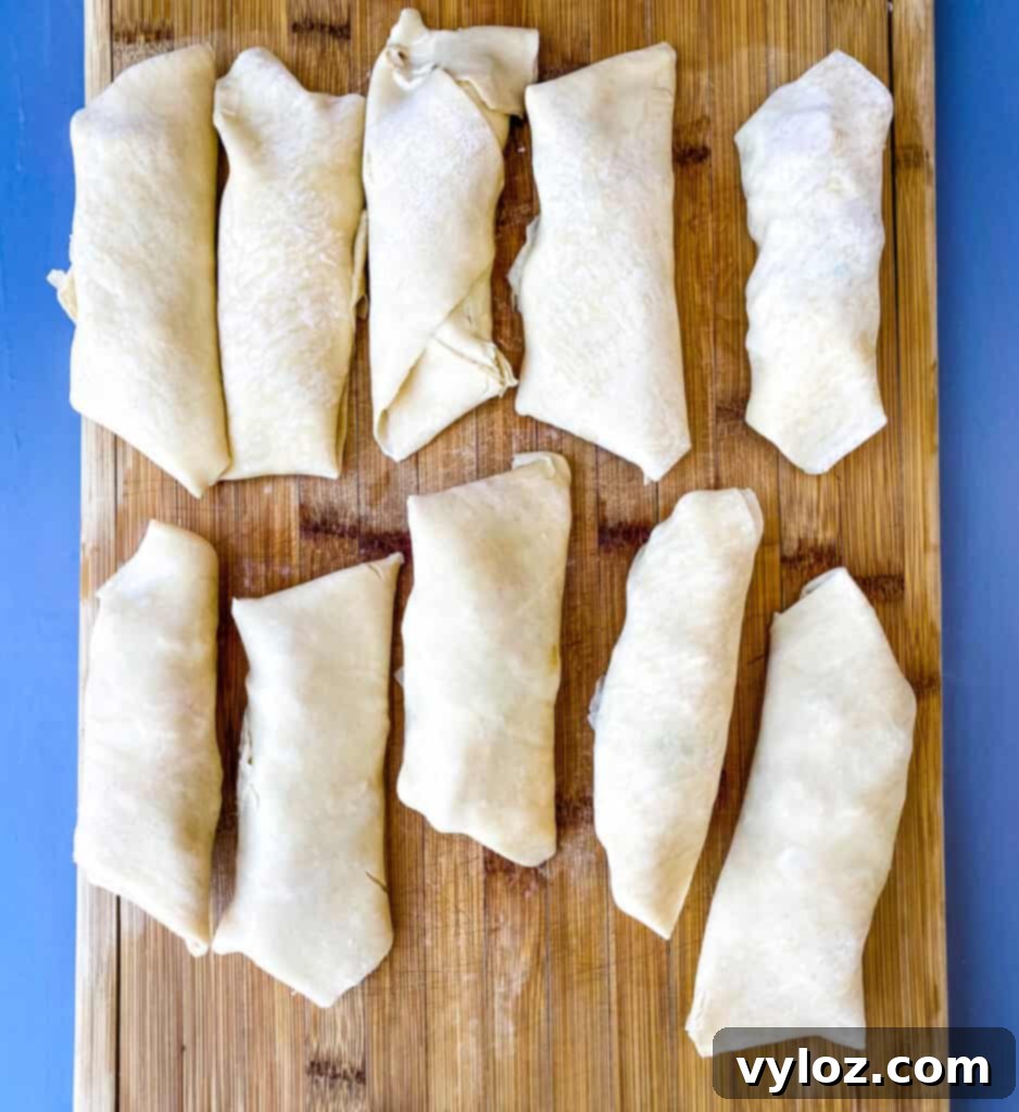 A batch of uncooked shrimp egg rolls neatly arranged on a cutting board, ready for baking or air frying.
