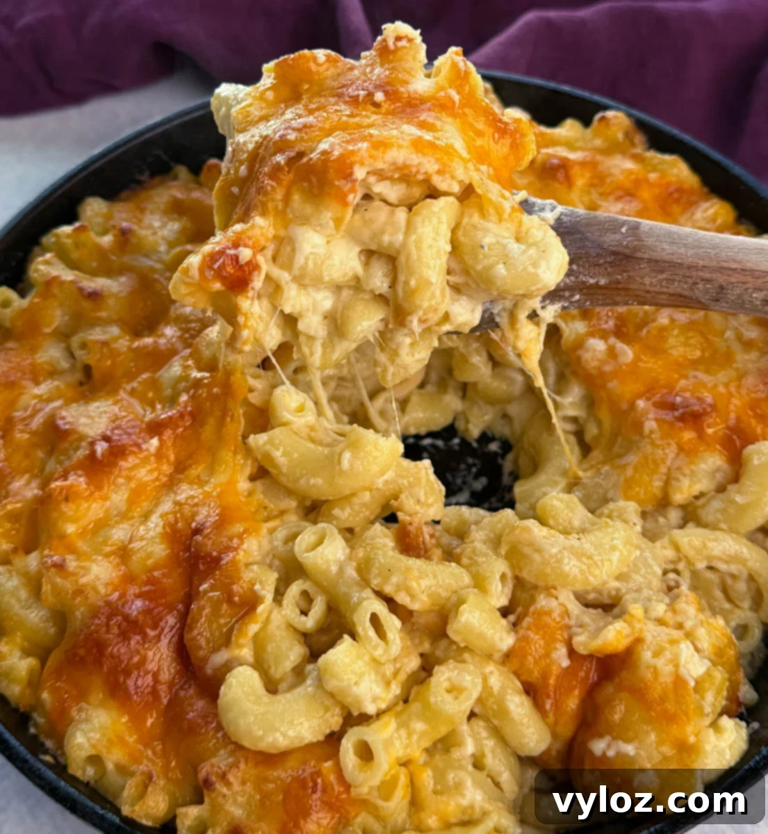 Soul-Satisfying Southern Baked Mac and Cheese 15 Close-up of a cast iron skillet filled with Southern baked mac and cheese, with a wooden spoon lifting a gooey serving showing melted cheddar cheese stretching.