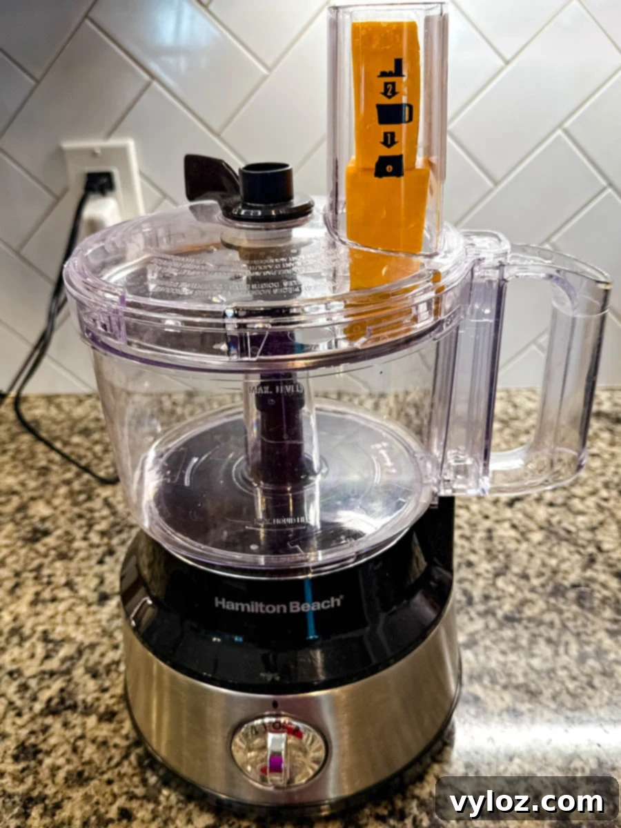 Soul-Satisfying Southern Baked Mac and Cheese 5 Food processor with a block of cheddar cheese in the chute, ready to be shredded.