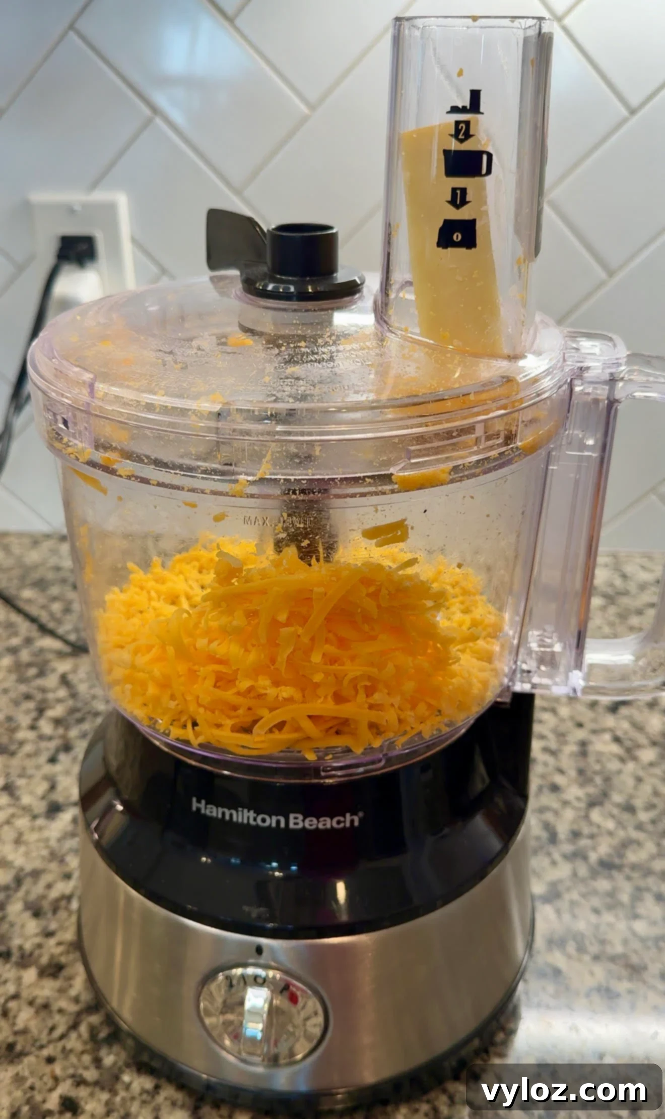 Soul-Satisfying Southern Baked Mac and Cheese 6 Food processor with a block of cheddar cheese in the chute, ready to be shredded.