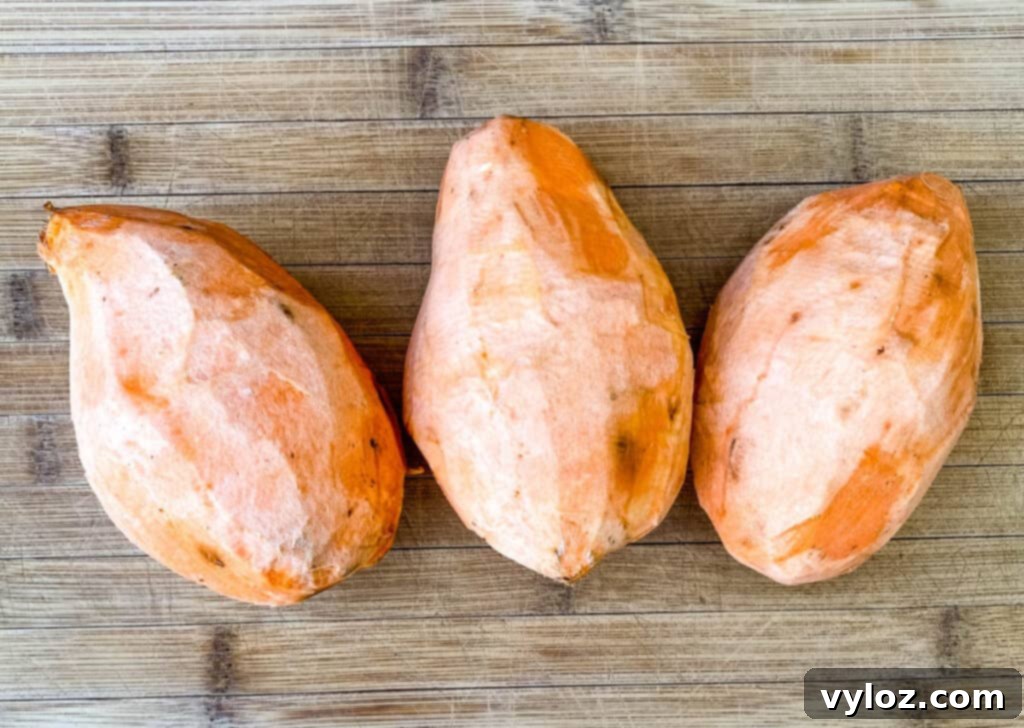 Crispy Air Fryer Sweet Potato Hash 3 Raw, unpeeled sweet potatoes on a bamboo cutting board, ready for preparation.