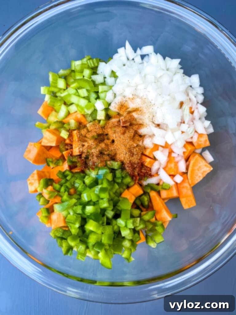 Crispy Air Fryer Sweet Potato Hash 6 Diced sweet potatoes, onions, green bell peppers, and celery in a clear glass bowl, ready for seasoning.