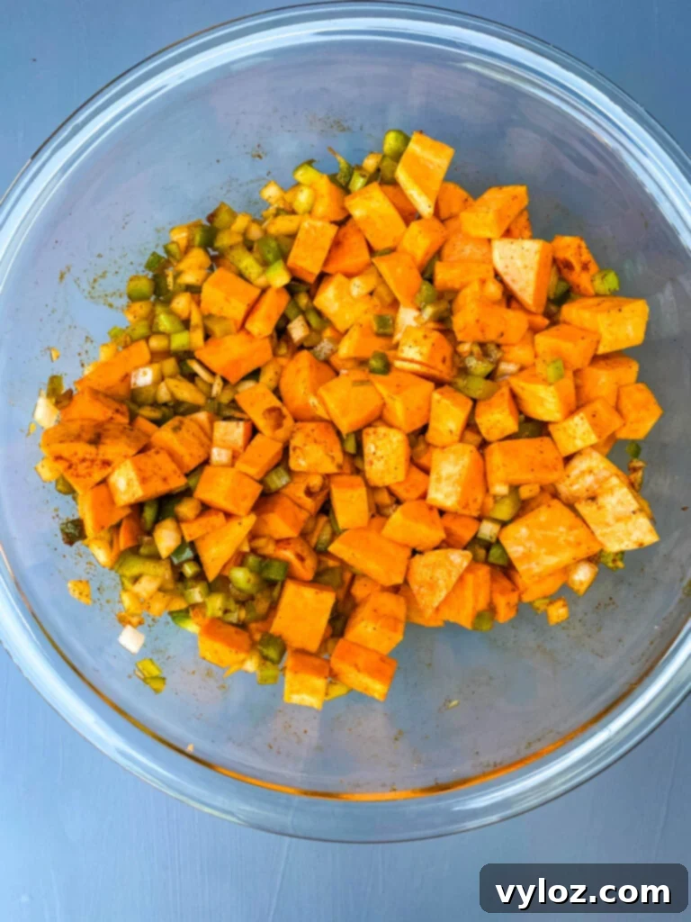 Crispy Air Fryer Sweet Potato Hash 7 Raw sweet potato hash mixture with vegetables and seasoning in a glass bowl, ready for the air fryer.