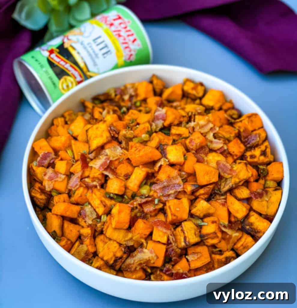 Crispy Air Fryer Sweet Potato Hash 10 A white bowl filled with air fryer sweet potato hash and crumbled bacon, with a bottle of Tony Chachere's Creole seasoning in the background.