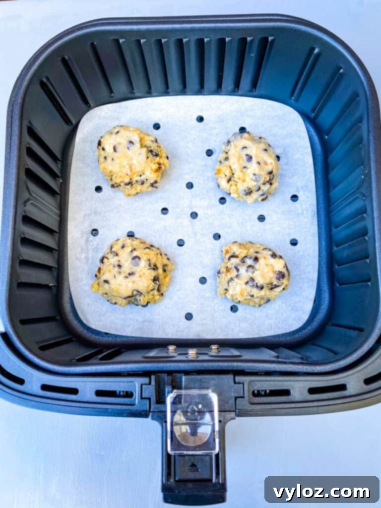 chocolate chip cookie dough balls arranged in an air fryer basket lined with parchment paper