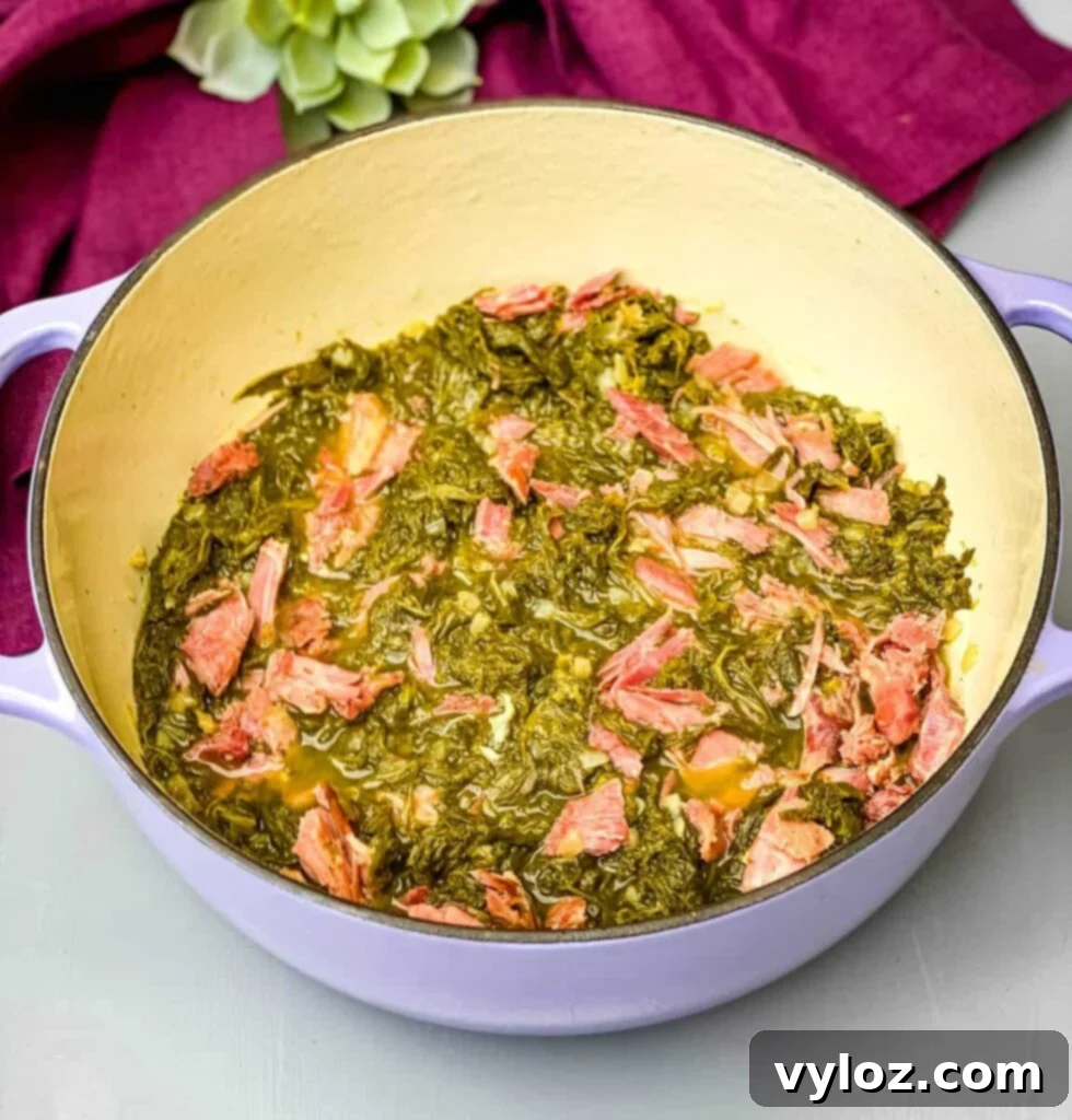 Cooked Southern mustard greens served in a Dutch oven with a smoked turkey leg, rich with savory juices.