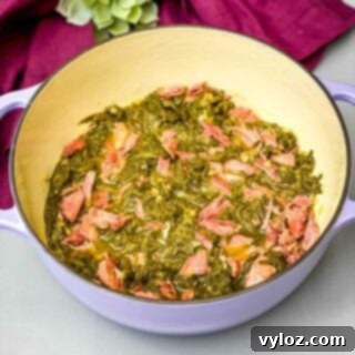 Cooked Southern mustard greens served in a Dutch oven with a smoked turkey leg, rich with savory juices.