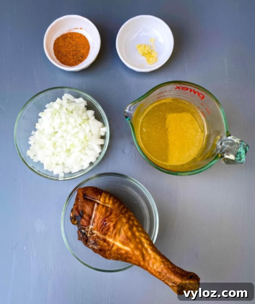 A flat lay image displaying essential ingredients for Southern mustard greens: Creole seasoning, fresh garlic, chopped onions, chicken broth, and a smoked turkey leg.