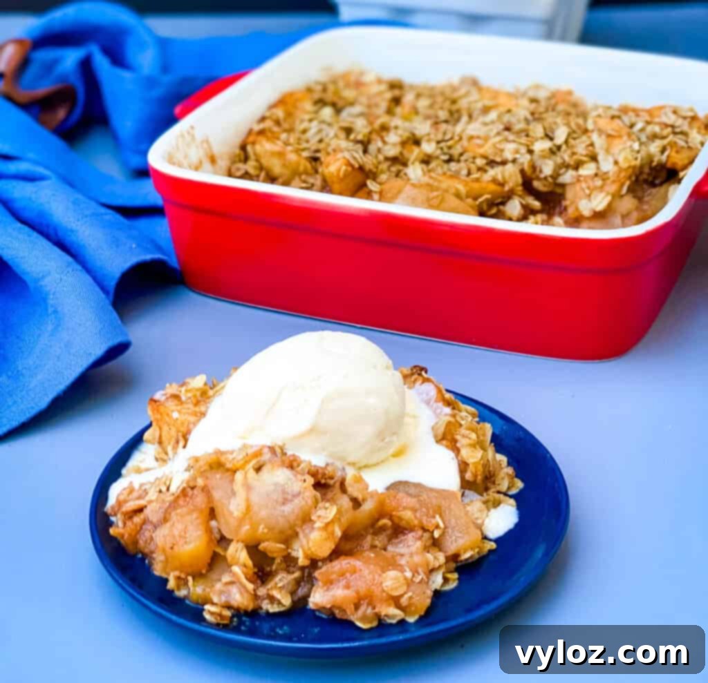 healthy apple crisp on a plate with a scoop of vanilla ice cream with a baking dish of crisp