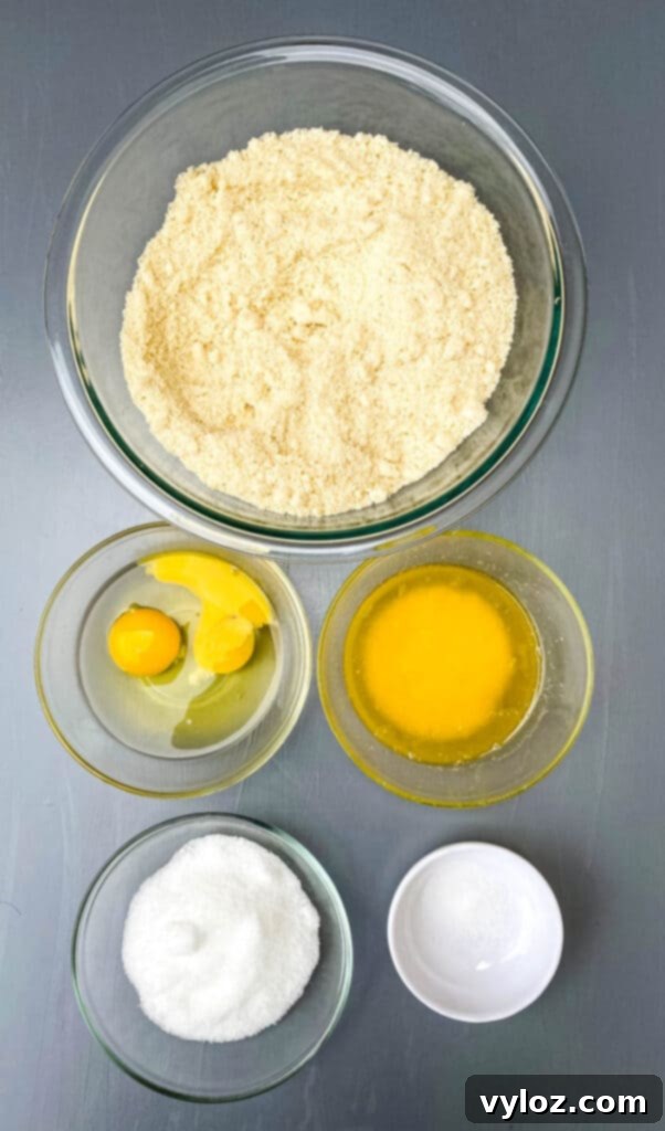 Almond flour, raw eggs, melted butter, sweetener, and salt in bowls on a flat surface, ingredients for almond flour crust