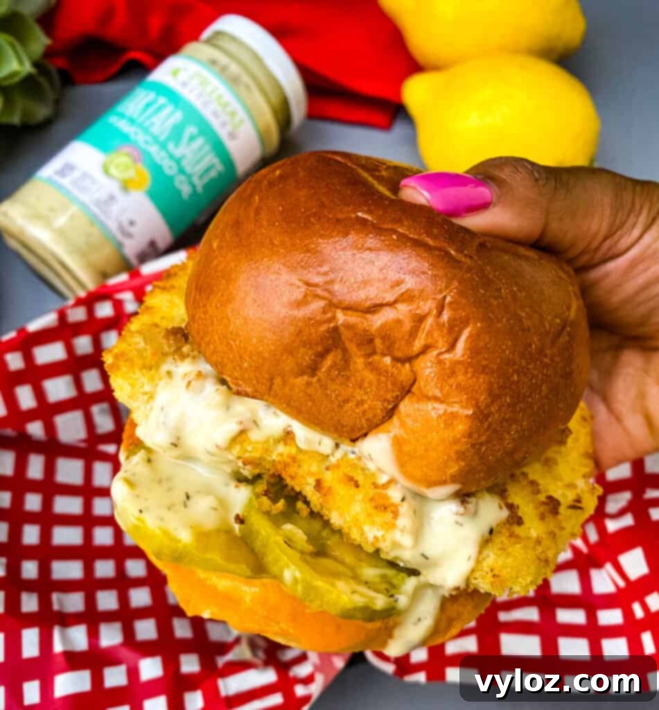 Crispy Air Fryer Fish Sandwich 10 Person holding a delicious air fryer fish sandwich on a bun with melted cheese and tartar sauce