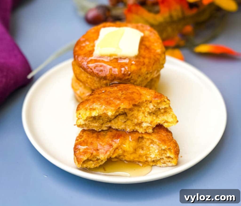 Deliciously Easy Sweet Potato Biscuits 13 A white plate with several sweet potato biscuits, one cut in half and drizzled generously with honey butter.