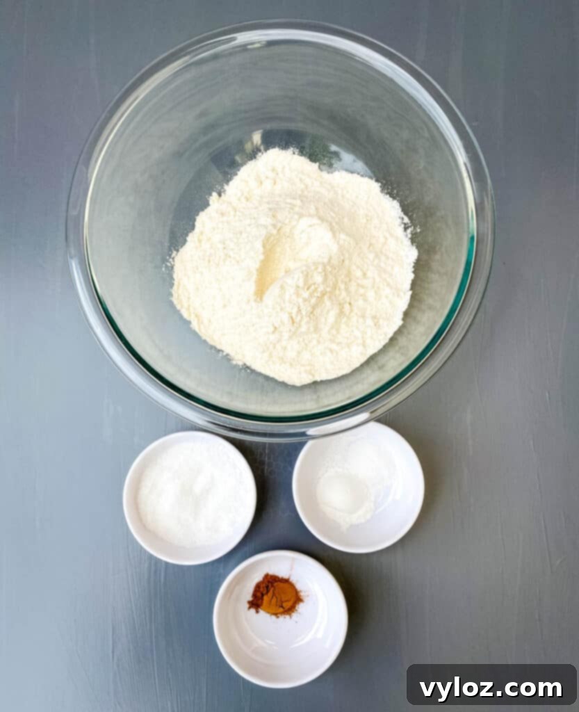 Deliciously Easy Sweet Potato Biscuits 4 Individual bowls containing baking essentials: flour, baking powder, salt, and ground cinnamon.