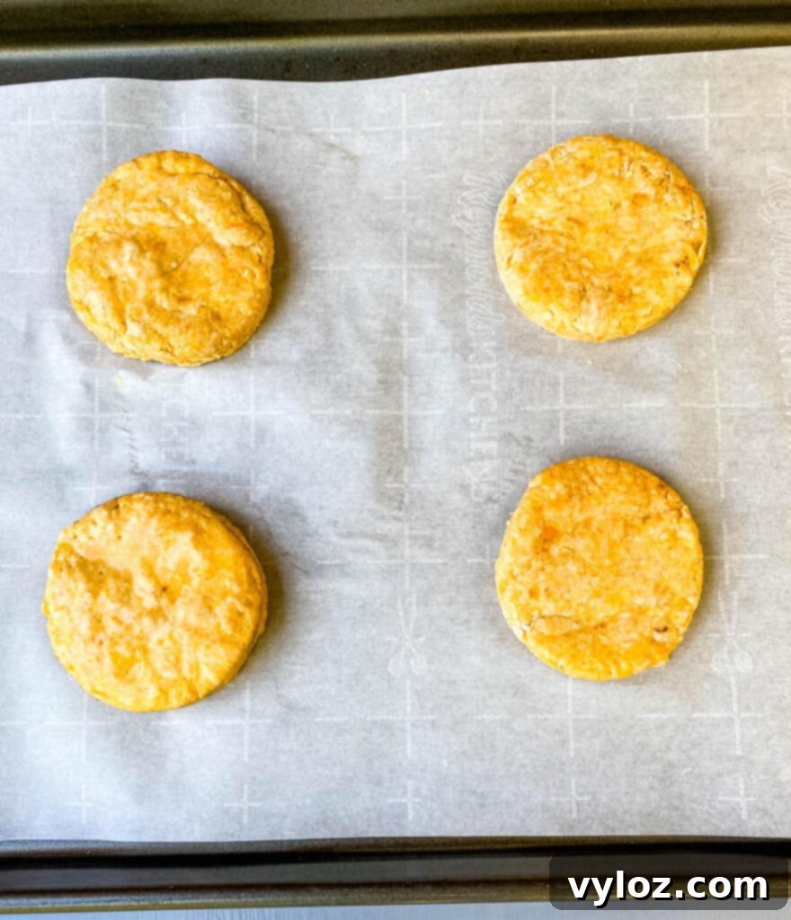 Deliciously Easy Sweet Potato Biscuits 8 Freshly baked sweet potato biscuits cooling on parchment paper on a sheet pan.