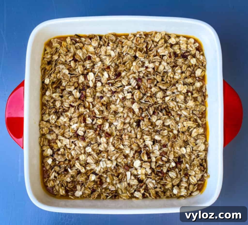 A beautifully baked healthy pumpkin crisp, boasting a golden-brown oat topping and a rich, creamy pumpkin filling, served fresh in a vibrant red baking dish, ready to be enjoyed.