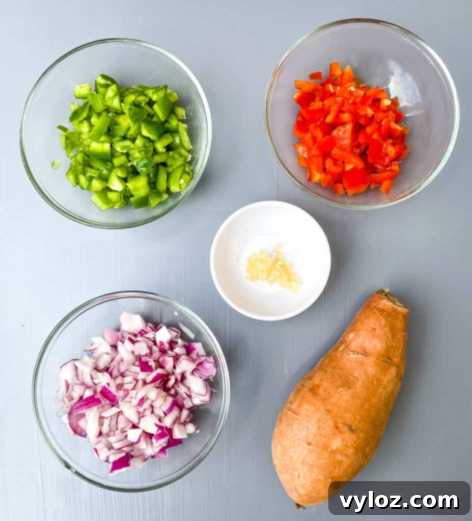 chopped green peppers, red peppers, onion, garlic, and a raw sweet potato on a flat surface