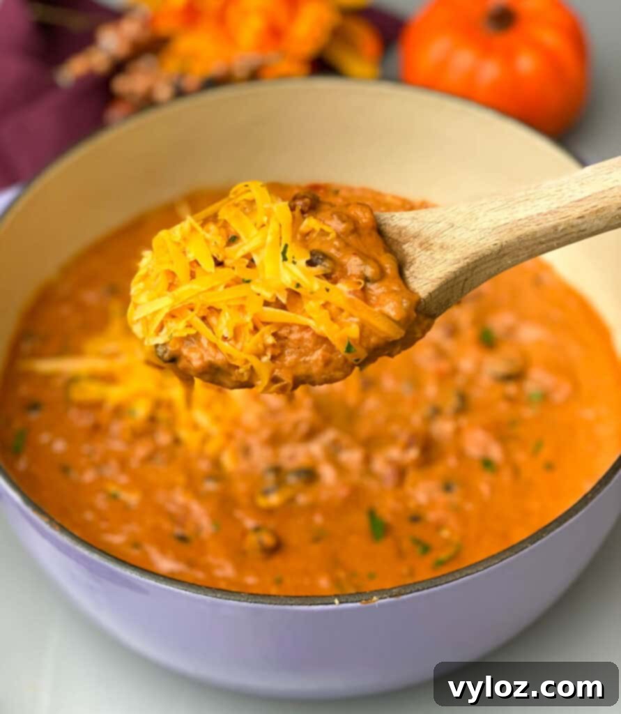 Autumnal Pumpkin Chicken Chili 11 A close-up of a spoon scooping a rich serving of pumpkin chicken chili from a white bowl, showcasing the hearty texture and inviting warmth of the dish.