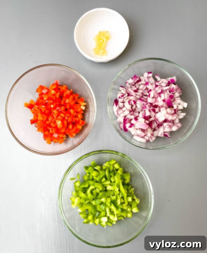 Autumnal Pumpkin Chicken Chili 3 A vibrant display of fresh, raw ingredients: green bell peppers, red bell peppers, neatly chopped onions, and garlic cloves, artfully arranged in separate bowls on a rustic wooden surface, ready for cooking.