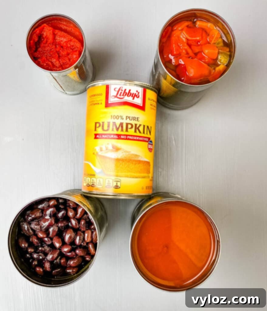 Autumnal Pumpkin Chicken Chili 4 A trio of essential canned ingredients for chili: black beans, diced tomatoes, and pure pumpkin puree, arranged on a kitchen counter, highlighting the convenience of pantry staples.